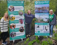 Fran, her daughter and granddaughter pose against banners for ShelterBox. 
